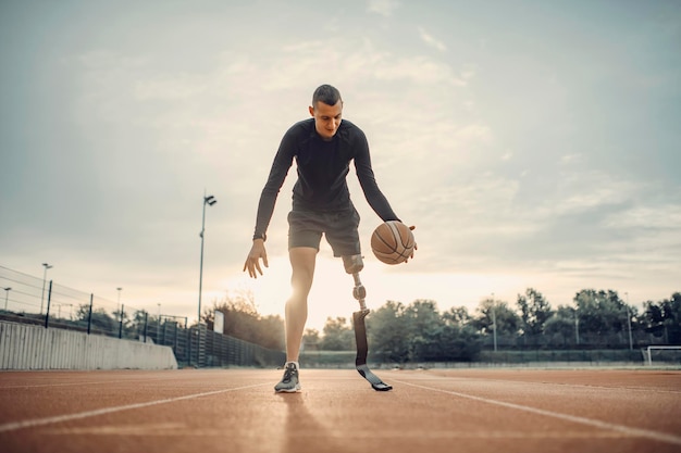 Een gehandicapte sportman met kunstbeen oefent basketbal in het stadion