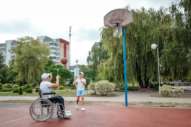 Een gehandicapte vader speelt met zijn zoon op straat. Rolstoelconcept, gehandicapte, vervullend leven, vader en zoon, activiteit, opgewektheid.