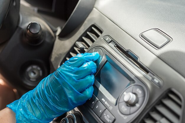 Een gehandschoende hand in de auto draait aan de volumeknop. Het dashboard in de auto. Detailopname.