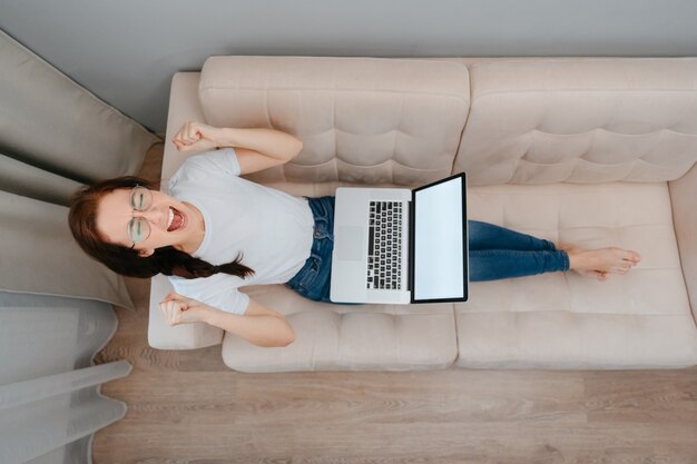 Een geïrriteerde studente die met een laptop op de bank zit, is overstuur door slecht nieuws onlinehet concept...