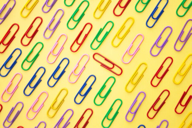 Een gele achtergrond met kleurrijke paperclips aan de bovenkant.