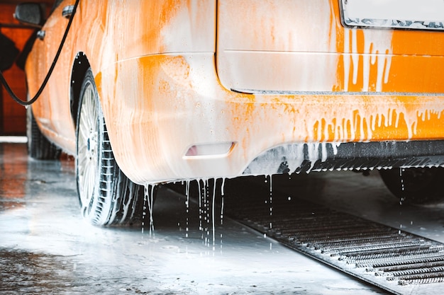 Een gele auto wassen bij een contactloze selfservice carwash Een sedan auto wassen met schuim en water onder hoge druk