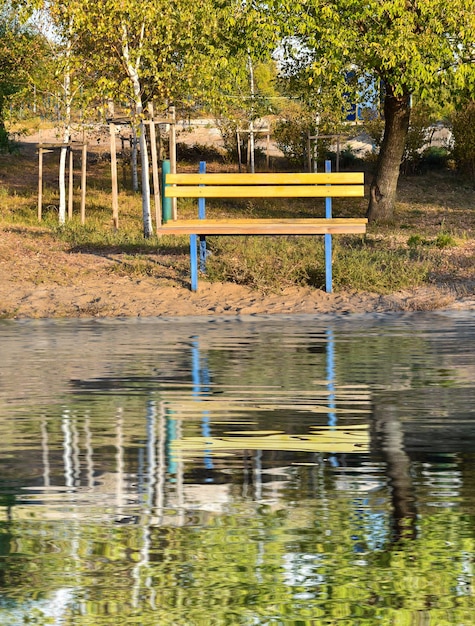 Een gele bank in het herfstpark wordt weerspiegeld in het water Mooie herfstachtergrond Eenzaamheidsconcept