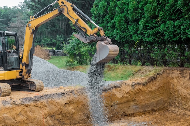 Een gele graafmachine emmer schop bewegende stenen grind van de stichting op een bouwplaats