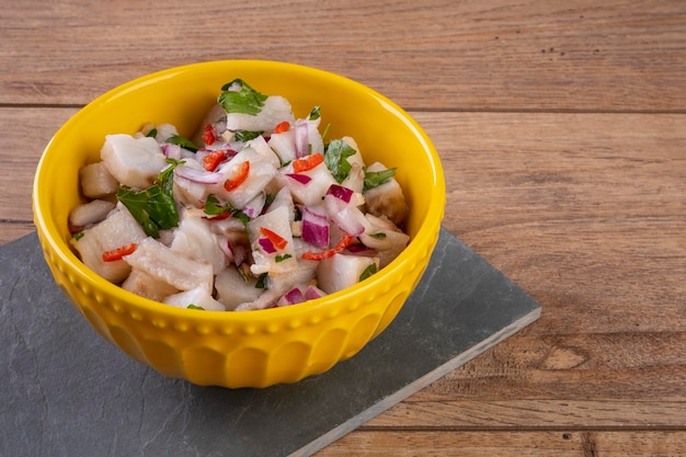 Een gele kom met ceviche op een houten tafel.