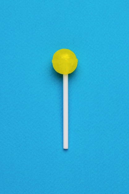 Foto een gele lolly op een stokje op een blauwe achtergrond minimaal concept van snoep