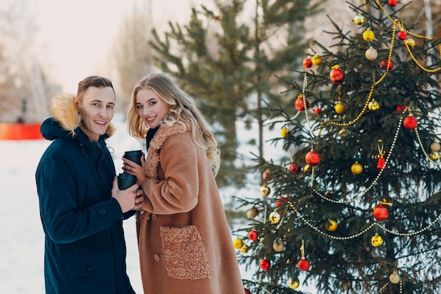 Een geliefd koppel drinkt koffie naast een versierde kerstboom in het winterbos.