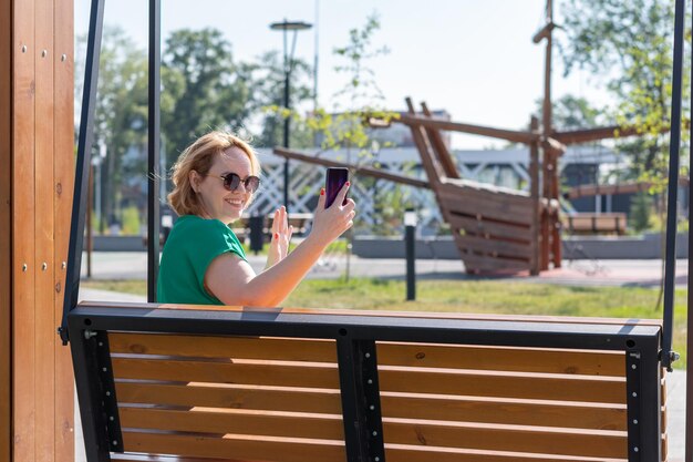 Een gelukkig, aantrekkelijk studentenmeisje met een zonnebril die een selfie-foto maakt op de telefoon terwijl ze met vrienden op straat praat