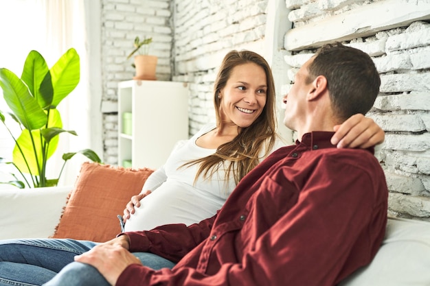Een gelukkig echtpaar, allebei veertig, dat een baby verwacht, straalt vreugde uit op hun gezellige bank thuis.
