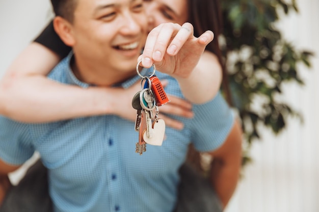 Een gelukkig getrouwd stel viert de verhuizing naar een nieuw huis laat zien dat de sleutels in een appartement staan, het concept van een hypotheek op vastgoedsleutels close-up