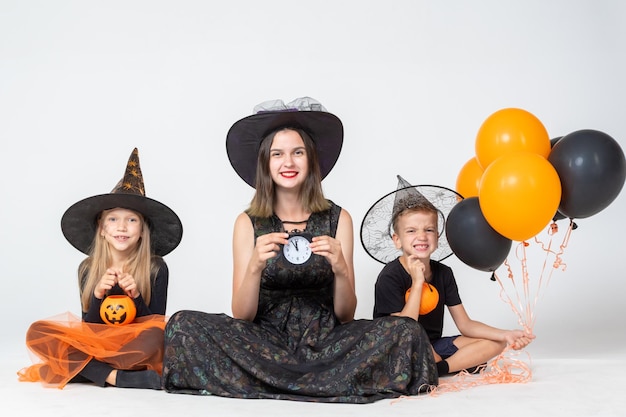 Een gelukkig gezin, een moeder en kinderen in griezelige heksen- en tovenaarskostuums met een zwarte horlogemand en ballonnen