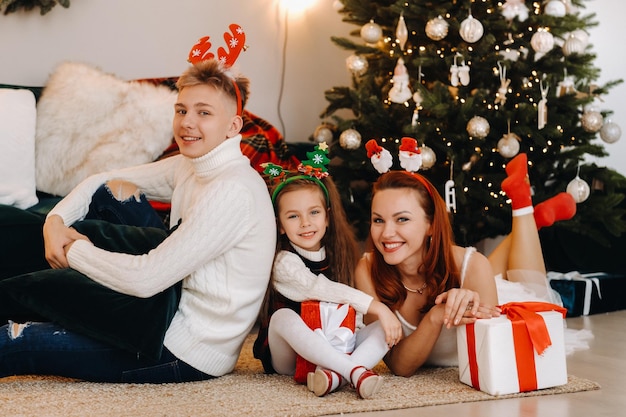 Een gelukkig gezin ligt op de vloer van het huis met nieuwjaarsgeschenken, naast de kerstboom