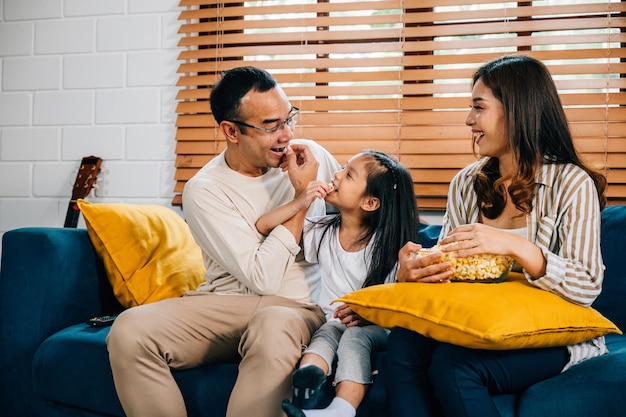 Een gelukkig gezin vol vreugde kijkt tv terwijl ze popcorn eten op een moderne bank thuis