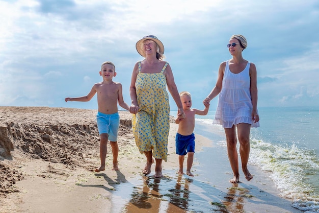 Een gelukkig gezin wandelt langs het zandstrand op een zonnige dag bejaarde vrouw moeder en kleine kinderen liefde en tederheid vakantie en reizen