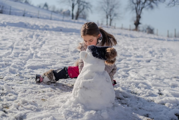 Een gelukkig jong geitje dat een sneeuwman maakt buiten kindmeisje dat buiten in de besneeuwde winter speelt.
