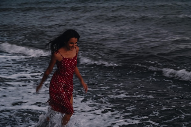 Een gelukkig jong meisje in een jurk rent op een zomeravond langs de golven van de zee op het strand