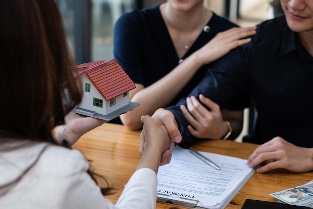 Een gelukkig jong stel ontvangt een prachtig koopje na ondertekening van een contract om een huis te kopen Makelaar en klant schudden de hand na een goede deal Vastgoedconcept