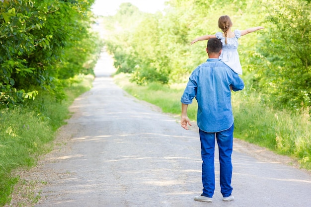 Een gelukkig kind met ouder op schouders loopt langs de weg op parkachtergrond