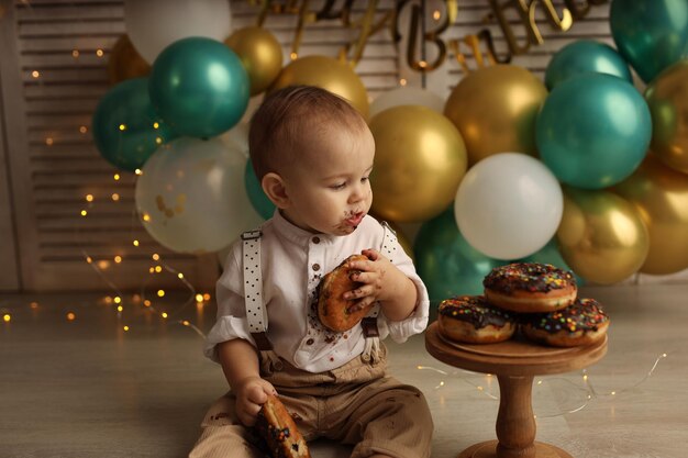 Een gelukkig kind op de achtergrond van ballonnen met slingers eet chocolade donuts Gelukkige verjaardag