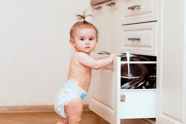Een gelukkig kind staat in de buurt van een open kast in de keuken. kind in de witte keuken. kind lacht in een witte keuken.