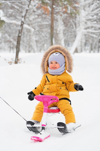 Een gelukkig kind van 1223 maanden oud lacht tijdens het rijden op een sneeuwkat voor kinderen in een winterpark