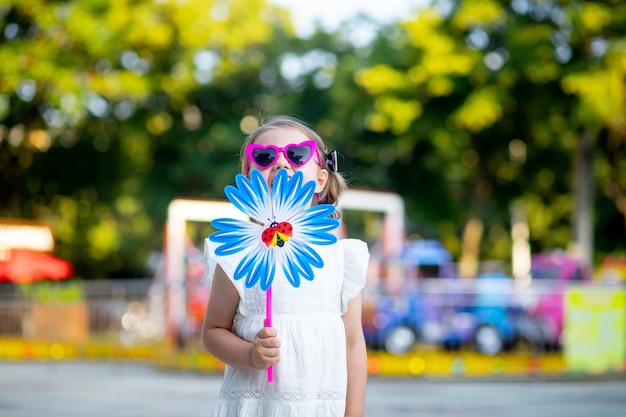 Een gelukkig kindmeisje lacht of lacht in een pretpark met een draaitafel in haar hand en een roze bril in de zomer