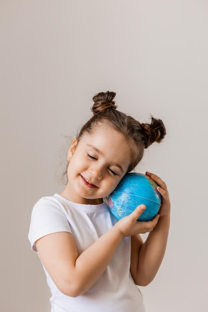 Een gelukkig klein meisje houdt een kleine bolplaneet in haar handen in een wit t-shirt op een wit