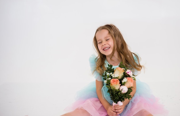 Een gelukkig klein meisje in een feestelijke jurk zit en houdt een boeket bloemen vast op een witte achtergrond met een kopie van de ruimte