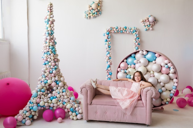 Een gelukkig klein meisje in een roze jurk ligt op een roze bank tussen ballonnen en torens. langverwachte reis naar Frankrijk