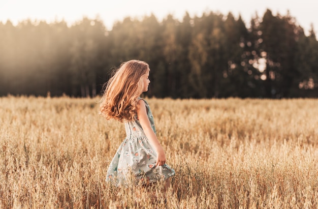 Een gelukkig klein meisje loopt in de zomer op een zonnige dag door een tarweveld. Zomertijd. Zomervakantie. Gelukkige jeugd. Positieve emoties en energie
