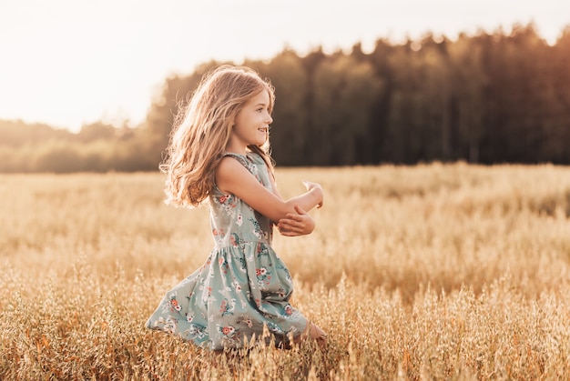 Een gelukkig klein meisje loopt in de zomer op een zonnige dag door een tarweveld. Zomertijd. Zomervakantie. Gelukkige jeugd. Positieve emoties en energie