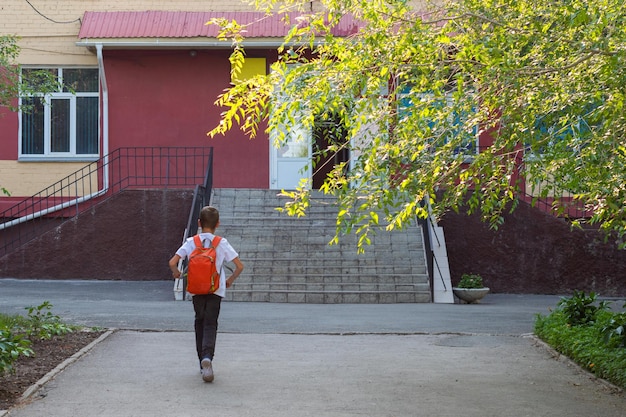 Een gelukkig lachend kind gaat naar school achteraanzicht van een jongen die buiten op trappen loopt om achtergrond te bouwen