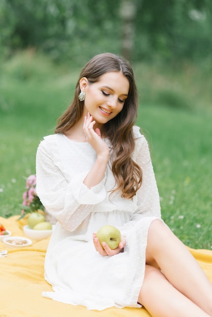 Een gelukkig lachend meisje houdt een appel in haar handen en zit op een gele deken tijdens een zomerpicknick buiten de stad