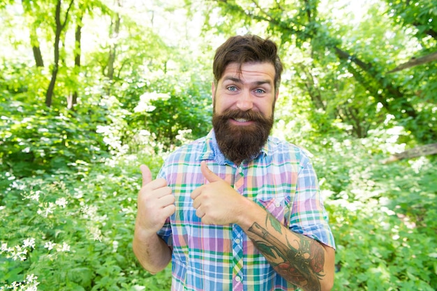 Een gelukkig leven leiden Gelukkige hipster die duimen omhoog gebaar op natuurlijk landschap geeft Emotionele kerel met lange snor en baardhaar op gelukkig gezicht Bebaarde man met gelukkige emoties in zomerstijl