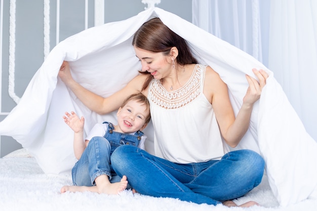 Een gelukkig, liefdevol gezin. Moeder en zoontje spelen thuis op het bed onder de deken.