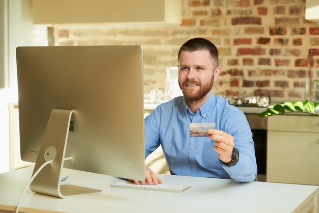 Een gelukkig man zit achter de computer en typt creditcardgegevens in een online winkel thuis