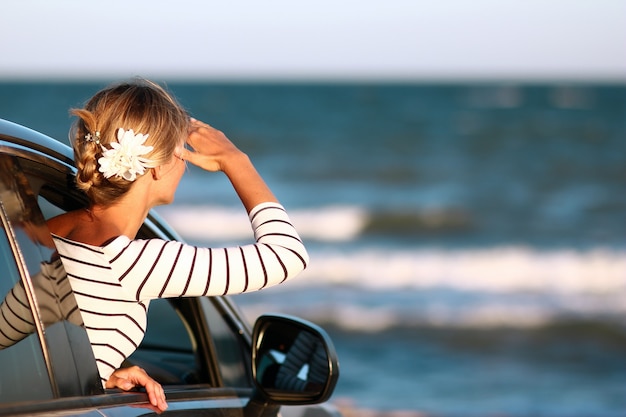 Een gelukkig meisje in de auto aan zee in de natuur op vakantiereizen