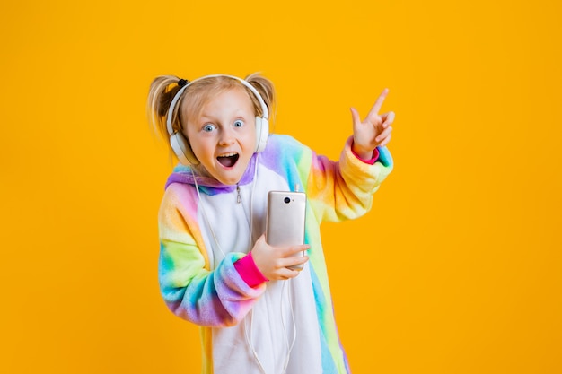 Een gelukkig meisje in een kigurumi-eenhoorn luistert naar muziek in hoofdtelefoons met een smartphone