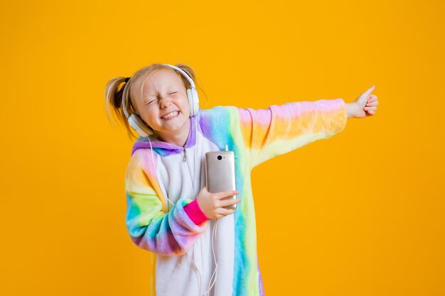 Een gelukkig meisje in een kigurumi-eenhoorn luistert naar muziek in hoofdtelefoons met een smartphone