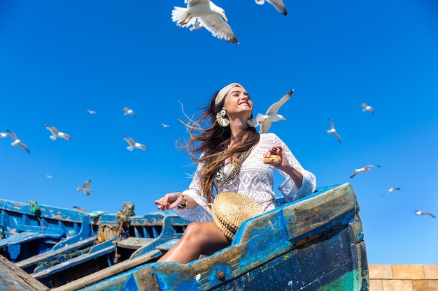 Een gelukkig meisje zit in een blauwe oude boot en voedt meeuwen. Essaouira. Marokko