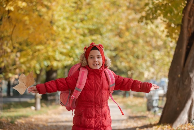 Een gelukkig moslimkind met een schoolrugzak die vrolijk door het herfstpark rent.