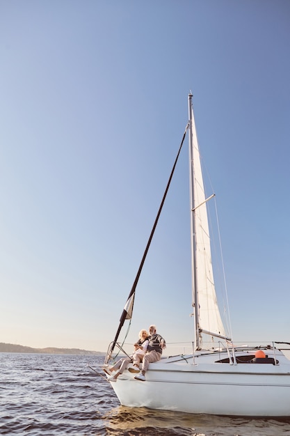 Een gelukkig senior paar praten zittend aan de zijkant van een zeilboot op een kalme blauwe zee man knuffelen zijn