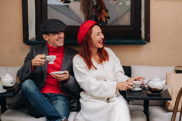 Een gelukkig stijlvol stel drinkt koffie en glimlacht terwijl ze in een café op straat zitten
