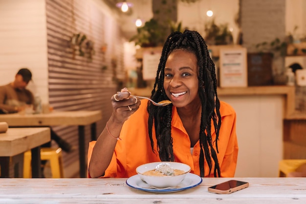 Een gelukkige Afro-Amerikaanse vrouw die aan een bar zit en een plantaardige spread eet Gezond voedselconcept