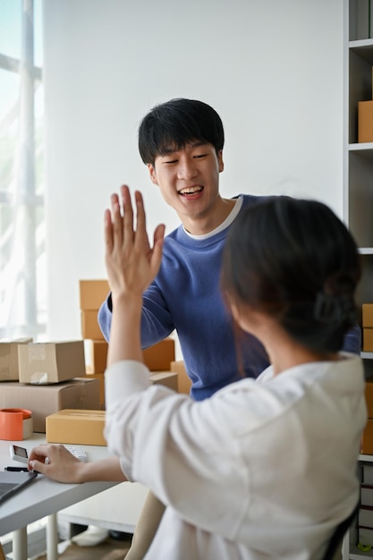 Een gelukkige Aziatische man geeft zijn vriendin een high five om hun online zakelijk succes te vieren