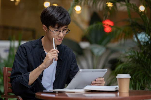 Een gelukkige Aziatische man werkt aan zijn digitale tablet aan een buitentafel in de koffieshop