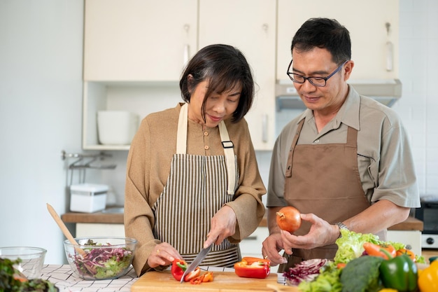 Een gelukkige Aziatische vrouw hakken een zoete peper terwijl haar man haar helpt in de keuken