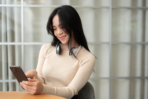 Een gelukkige Aziatische vrouw praat graag met haar vrienden op haar telefoon terwijl ze zich ontspant aan een tafel