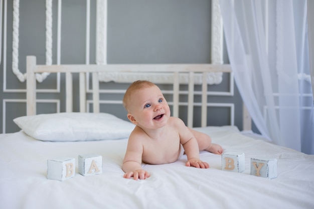 Een gelukkige babyjongen in een luier ligt op een witte deken op een bed met witte blokjes en kijkt naar de camera