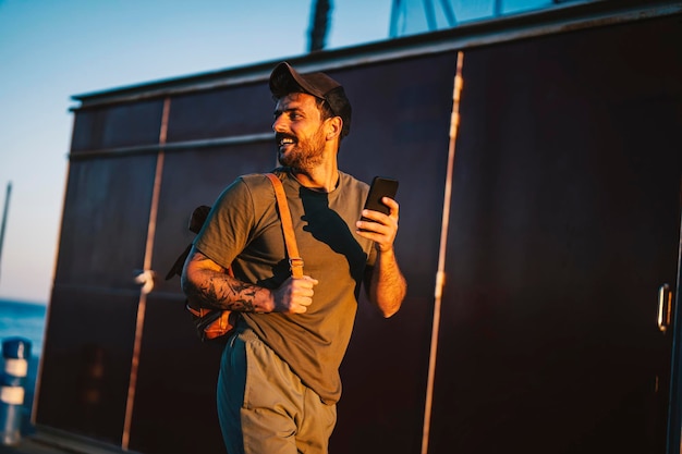 Een gelukkige casual man die met zijn telefoon op het dok loopt